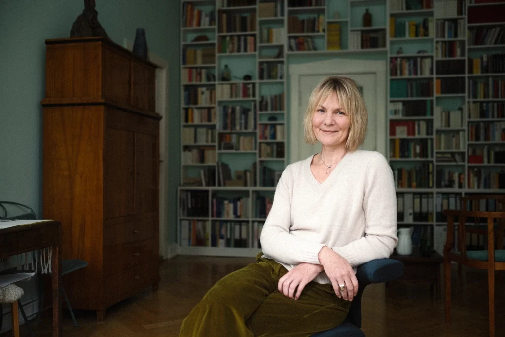 Gesa aufrecht sitzend vor Bücherwand